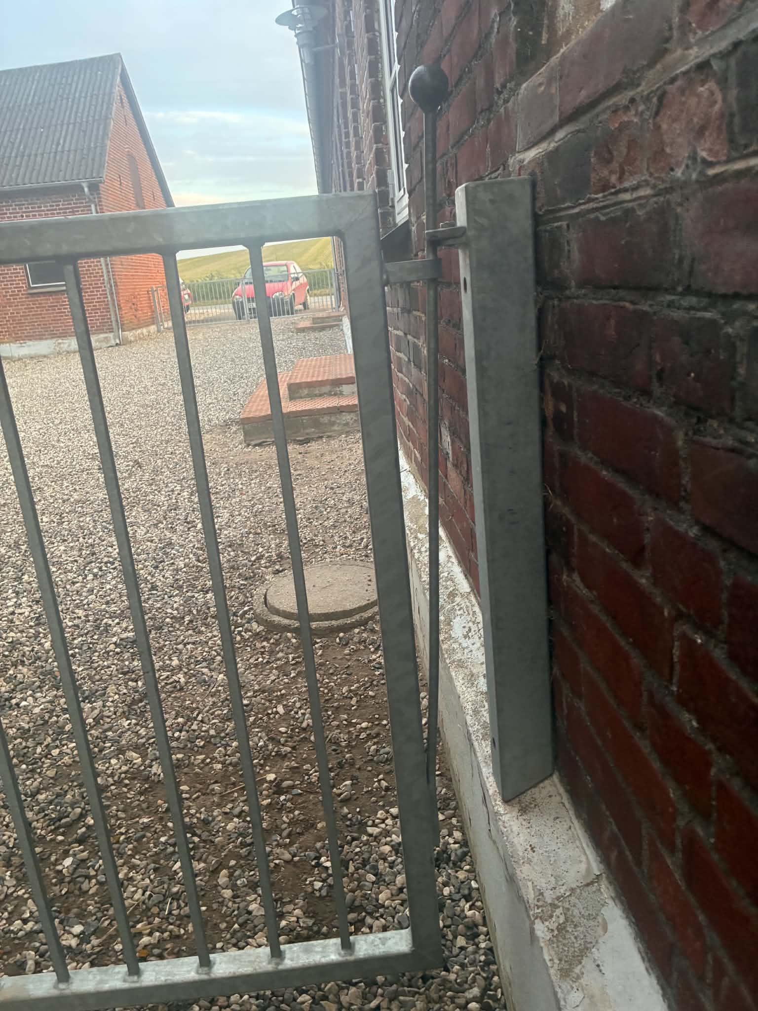 Fjederstangslås med sort knop over lågen, modbeslag på stolpen og en lang stang fastgjort ved bunden